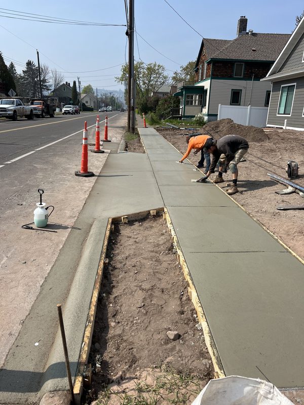 Crew pouring sidewalk in Duluth neighborhood with Lake Superior in distance