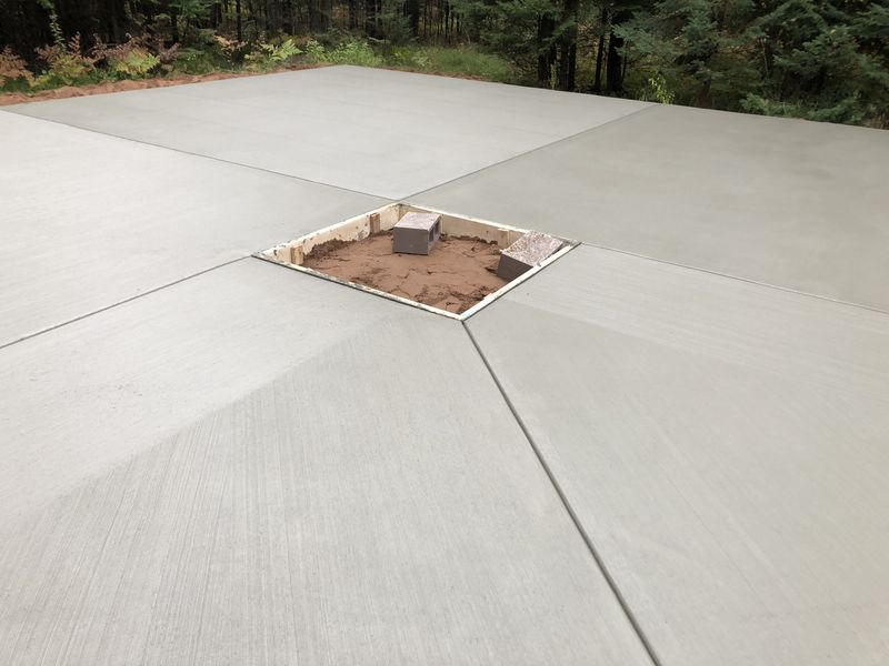 Large finished concrete patio with built-in fire pit opening and saw-cut control joints