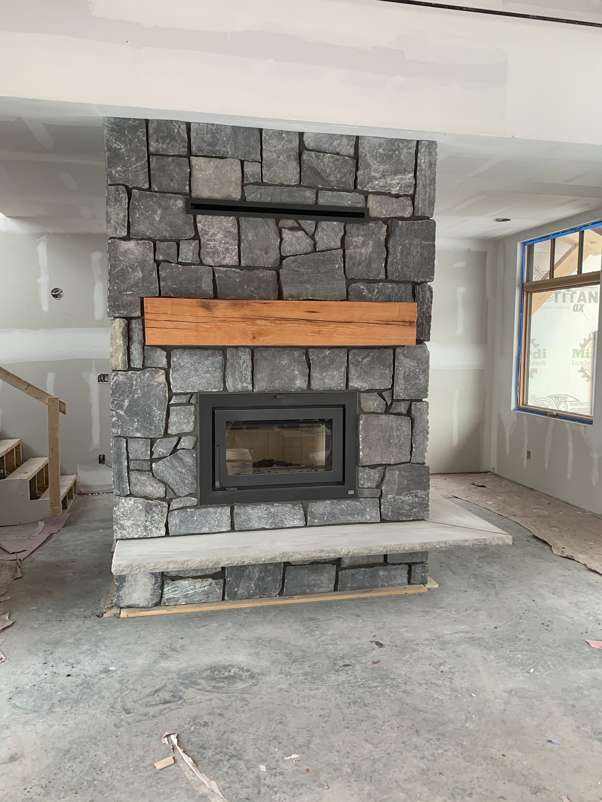 Custom natural stone fireplace with wood mantel built by Primetime Concrete